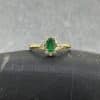 Anillo de oro amarillo de 18k con esmeralda ovalada de 0.56 cts rodeada por un halo de 14 diamantes brillantes de 0.20 cts en total sobre fondo blanco neutro.
