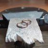 Fotografía original de Joyería Zayro que muestra una pareja de alianzas de boda de oro rosa de primera ley sobre la astillera de madera de una mesa de taller de joyería. Los anillos presentan un perfil media caña y fino de 2 mm de ancho con acabado pulido brillo reflectante, capturados de cerca con luz ambiental de taller que resalta el color cobrizo del metal y las texturas de la madera artesanal.