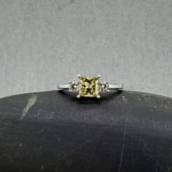 Anillo de pedida de oro blanco con diamante amarillo princesa y piedras laterales.