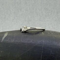 mer plano técnico del anillo de oro blanco asimétrico Hermes; detalle de la montura de cuatro garras y los brazos que envuelven de arriba a abajo un diamante natural redondo de 0.20 cts, colocado sobre el fondo mineral gris de un canto rodado.
