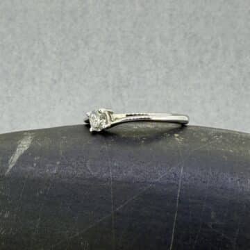 mer plano técnico del anillo de oro blanco asimétrico Hermes; detalle de la montura de cuatro garras y los brazos que envuelven de arriba a abajo un diamante natural redondo de 0.20 cts, colocado sobre el fondo mineral gris de un canto rodado.