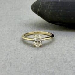 Anillo de compromiso solitario Venus en oro amarillo con un diamante de laboratorio oval central, expuesto sobre la astillera de madera texturizada del taller de Joyería Zayro en Zaragoza, mostrando la escala real de la joya junto a sutiles marcas de herramientas artesanales.