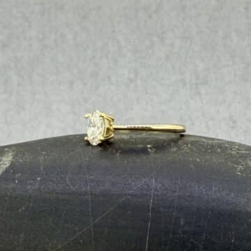 Primer plano de perfil de un anillo de compromiso de oro amarillo de 18k; detalle macro de la montura Venus que eleva un diamante oval de laboratorio sujeto por cuatro garras sobre un brazo con perfil de cuchilla, sobre fondo neutro.